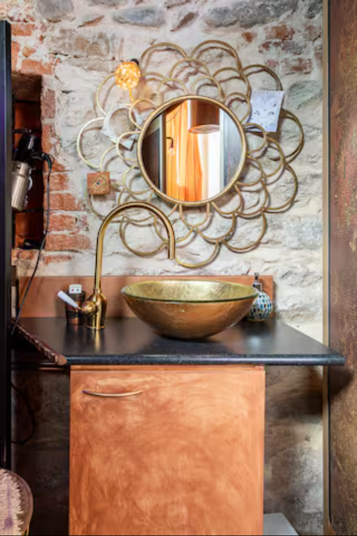 Bagno di CasaRosada con lavabo in vetro dorato e muro in pietra